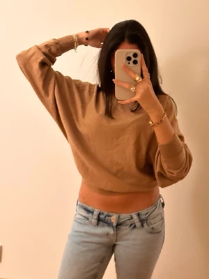 Beige croppad tröja med vida ärmar - Säljer en beige croppad tröja med breda, avslappnade ärmar och ribbad mudd i midjan och vid ärmsluten. Perfekt för en chill och trendig look. Tröjan har en enkel design utan synligt märke och är gjord i ett mjukt material.