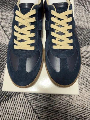 Marinblå sneakers med mockadetaljer - Snygga marinblå sneakers med ovandel i mocka och skinn, beige snörning och klassisk gummisula. Skorna har en stilren design med rund tå och kontrasterande materialval som ger en modern look.