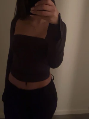 Mörkgrå långärmad tubtopp - Säljer en mörkgrå tubtopp med långa ärmar och axelbandslös design. Toppen har en croppad passform och är tillverkad i ett mjukt, stretchigt material som sitter snyggt mot kroppen. Perfekt för dig som gillar minimalistisk och trendig stil.