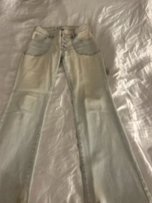 Ljusblå lågmidjade flare jeans med knappar - Säljer ett par ljusblå jeans med raka ben och synliga knappar framtill. Jeansen har klassiska fem fickor och en cool, tvättad look. Perfekta för dig som gillar en avslappnad och trendig stil.