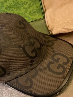 Gucci keps - Säljer en snygg keps från Gucci i svart tyg med det klassiska GG-monogrammet över hela kepsen. Kepsen har böjd skärm och svarta detaljer längs kanten. Perfekt för dig som vill ha en exklusiv och trendig accessoar.