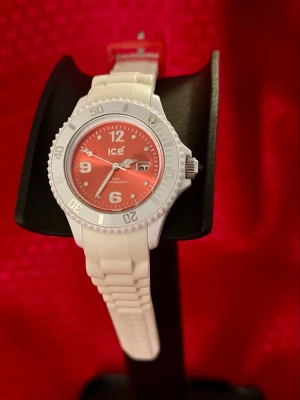 ICE Watch vit och orang klocka  3,5 cm diameter  - Snygg klocka från ICE Watch med vit silikonrem och röd urtavla. Klockan har tydliga siffror, datumvisning och en sportig look. Detaljer i silver och en röd detalj på remmen gör den extra unik. Perfekt accessoar för dig som vill sticka ut.