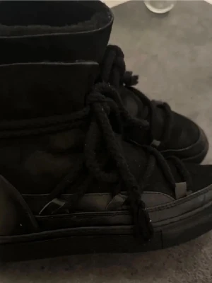 Svarta Inuikii skor  - Snygga svarta boots ifrån inuiiki med hög skaft och snörning. Skorna har en robust sula och är tillverkade i  mocka. Perfekta för kyligare väder med en stilren design. Använda men fortfarande i fint skick, liten inböjning vid hälen men inget som påverkar skon