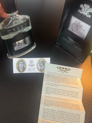 Creed Aventus  - Lyxig parfym från Creed, Aventus, med elegant glasflaska och svart etikett med silverdetaljer. Flaskan har en unik form och levereras med originalkartong och informationsblad. En ikonisk doft för den som vill sticka ut.