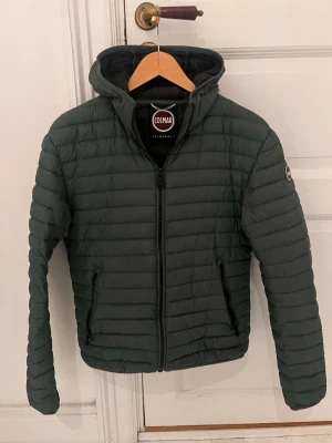 Grön Colmar jacka med huva - Säljer en fin vår jacka i mårket colmar, mörkgrön med huva och dragkedja framtill. Jackan har två fickor med dragkedja och ett Colmar-märke på. perfekt för varma vår dagar till kalla höstdagar. Snygg, quiltad design och riktigt skön passform. Passar 155-165 Växte ur den precis och jag är 170 (storlek 46, motsvarar s/xs