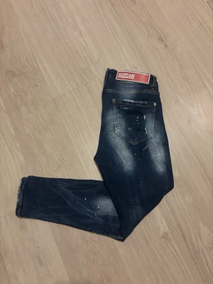 Dsquared2 jeans  - Snygga mörkblå jeans från Dsquared2 med slitningar och färgstänk för en cool look. Jeansen har klassisk femficksdesign, smal passform och tydlig Dsquared2-logga på framsidan och bakfickan. Perfekt för dig som vill ha en unik och snygg stil. Hör av dig vid frågor!