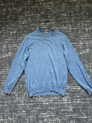 Blå stickad tröja från Oscar Jacobson - Snygg blå stickad tröja från Oscar Jacobson med rund halsringning och ribbade muddar vid ärmslut och nederkant. Perfekt för lager på lager och enkel att matcha med jeans eller chinos. Materialet är mjukt och bekvämt.