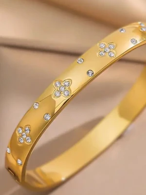 Guldfärgat armband med blommönster - Snyggt guld pläterad armband i metall med blommönster av små gnistrande stenar. Armbandet har en slät, blank yta och dekoreras av flera blommor och enstaka stenar som ger en exklusiv känsla. Perfekt accessoar för att lyfta din stil. Den är stålfri