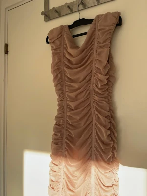 Champagnefärgad omlottklänning från ZARA - Supersnygg champagnefärgad kortklänning från ZARA med omlottdesign och markerade axlar. Klänningen har ett rynkat tyg som ger en cool och trendig look. Perfekt för dig som vill sticka ut lite extra. Materialet känns mjukt och följsamt.