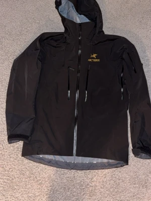 Svart Arc'teryx Gore-Tex regnjacka - Arc'teryx alpha i storlek M. Tillverkad i slitstark Gore-Tex Pro som står emot både regn och vind. Om ni har några frågor så får ni gärna ställa frågor. Kan skicka om ni står för frakten. Jag köpte den begagnad så kan ej garantera att den är äkta men har ytterst svårt o tro att den är fejk med tanke på alla detaljer. Den har även spårningssystmet Rocco som andvänds om du fastnar under snön.