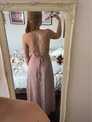Ljusrosa långklänning med snörning - Säljer en elegant ljusrosa långklänning med öppen rygg och snygg snörning bak. Klänningen har tunna axelband som korsas i ryggen.