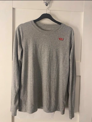 Grå långärmad tröja från Levi's - En stilren grå långärmad tröja från Levi's med rund halsringning och den klassiska röda Levi's-loggan på bröstet. 