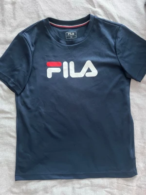 En mörkblå sport fila t shirt - En fila t shirt med sport material som är väldigt luftig och andas. Passar till när man ska träna eller bara ha en lugn dag.