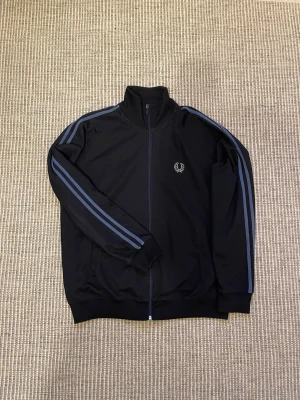 Fred Perry Tracktop  - En fräsch Fred Perry tracktop/zip up som jag nu säljer pga storlek. Ny pris ligger runt 900kr-1500kr. Den är storlek L men skulle säga att den sitter lite mer som en M. 