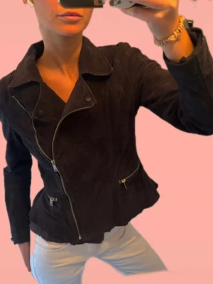 Mockajacka svart med coola detaljer och volang   - Supersnygg skinnjacka/bikerjacka från Jessica C&A!! Svart med coola detaljer och som en liten volang vid slutet av jackan. 100% mocka/skinn. Figursydd och köpt i storlek 38, S/M😍😍❤️❤️Kan skicka redan idag!