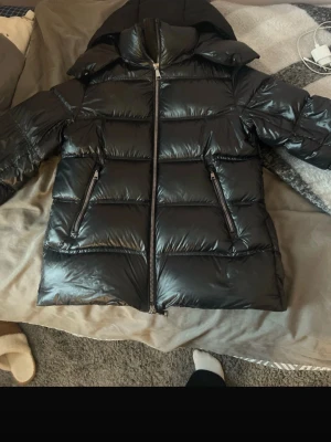 Svart pufferjacka från Massimo Dutti - Säljer en svart pufferjacka från Massimo Dutti med huva och blanka paneler. Jackan har dragkedja framtill och två snedställda fickor med dragkedja. Perfekt för kalla dagar och riktigt snygg till vintern. Även lite stor i storleken