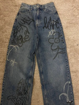 ”Graffiti” jeans från H&M - Jeans med design av graffiti från H&M i blå färg. Storlek 34. Aldrig använt den förut. 