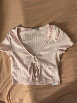 Ljusrosa croppad topp - Söt ljusrosa croppad topp hjärt-detaljer och v-ringning. Toppen har korta ärmar och knappar framtill.