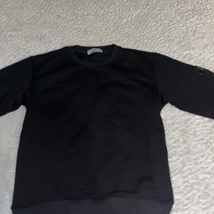 Svart Stone Island sweatshirt - Svart sweatshirt från Stone Island med klassisk rund hals och ikonisk logotyp-patch på vänster ärm. Tröjan är nästan aldrig använd och är i nyskick. Tröjan är i mjuk bomull och har ribbade muddar vid ärmslut och midja. Perfekt för en clean och stilren look. Priset är inte hugget i sten, men tycker priset är bra jämfört med nypris och skicket den är i.