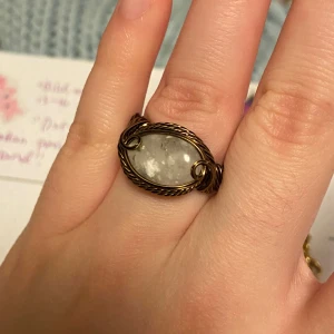 Handgjord ring med vit sten - Unik ring med en oval, vit sten infattad i tvinnad metalltråd i antik bronsfärg. Stenen har naturliga mönster och ringen har snygga snirkliga detaljer på sidorna. Perfekt för dig som gillar boho eller vintage vibes. Stenen hittade jag på Sicilien och har polerat den själv. 