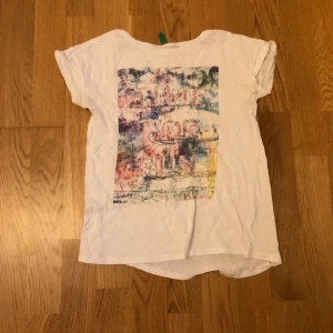 Vit t-shirt med färgglatt tryck typ 146-152 - Vit t-shirt med korta ärmar och ett stort färgglatt tryck på framsidan där det står 'TIME FOR FUN' i pastelliga nyanser. Trycket har en konstnärlig, lite sliten look med inslag av blått, rosa, lila och gult. Skön och avslappnad passform, perfekt för en chill stil. Mjukt tyg och är från Benetton.