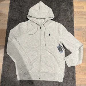 Ljusgrå Ralph lauren zip hoodie - Säljer nu denna riktigt feta Ralph lauren zip Hoodien i nyskick. Storlek M. Han på bild är 185cm, 74kg. Qr koden scannar till Ralph lauren hemsidan. Pris kan diskuteras vid snabb affär!