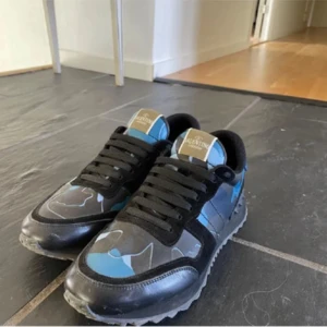 Valentino Rockrunner sneakers blå/svart - Snygga Valentino Rockrunner sneakers med blå och svarta camouflage-detaljer. Skorna har rund tå, svarta snören och en platt sula med grovt mönster. Materialmix av skinn och syntet, perfekt för dig som gillar streetstyle och exklusiva märken. Knappt använda! Mitt pris 2800!