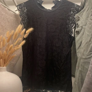 Svart spetsblus med detaljer - Säljer en svart blus i spets med vackra broderade detaljer och korta ärmar. Blusen har rund halsringning och ett feminint, luftigt mönster i tyget. Perfekt att styla med jeans eller kjol för en trendig look | skriv vid intresse💕