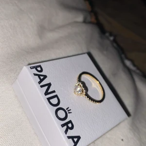 Guldfärgad hjärtring från Pandora/kvitto finns - Superfin guldfärgad ring från Pandora med ett gnistrande hjärta i mitten och små stenar runt hela ringen. Perfekt för dig som vill ha något extra glittrigt och romantiskt på fingret.