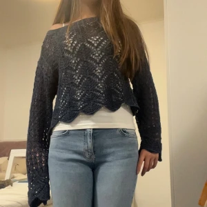 Mörkblå virkad stickad tröja - Säljer en mörkblå virkad stickad tröja med snyggt mönster och vågig nederkant. Tröjan är lite croppad och har långa ärmar samt offshoulder-passform. Perfekt att styla över ett linne eller t-shirt för en chill look.