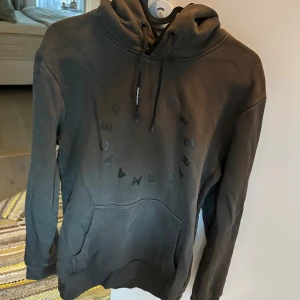 Svart hoodie från Peak Performance - Säljer en svart hoodie från Peak Performance med diskret logga i cirkel på bröstet. Tröjan har huva med snörning och en stor magficka. Perfekt för dig som gillar en clean och stilren look.