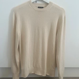 Beige stickad tröja från Massimo Dutti - Snygg beige stickad tröja från Massimo Dutti i en mix av bomull och ull. Tröjan har rund halsringning, ribbade muddar och lång ärm. Perfekt för lager-på-lager och enkel att matcha med jeans eller chinos.