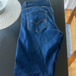 Mörkblå jeans från Morris 31/32 - Snygga mörkblå jeans från Morris i klassisk femficksmodell. Jeansen har guldfärgad broderad lilja på myntfickan och kontrastsömmar. Tillverkade i mjukt bomullstyg med stretch för extra komfort. Har ett hål i högra fickan de är de ända. 