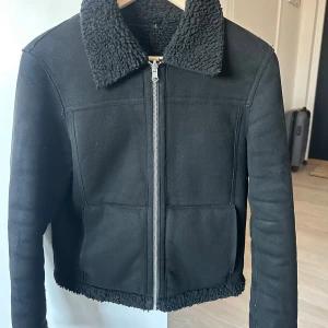 Svart teddyjacka med dragkedja - Svart teddyjacka med mjuk fuskpäls på krage och insida. Jackan kan även vända ut och in för att få fuskpälsen utanför. 