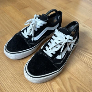 Svarta Vans Old Skool sneakers - Klassiska Vans Old Skool sneakers i svart med vit sidorand och vita snören. Storlek 43, väldigt bra skick. Men en liten skada, syns knappt men finns på bild. 