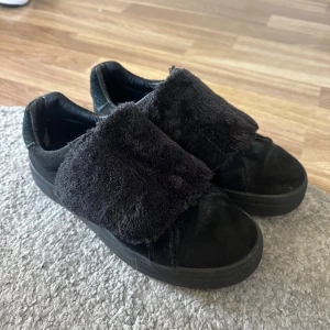 Svarta sneakers med fuskpäls och kardborre från ICHI - Unika svarta sneakers från ICHI med breda band i mjuk fuskpäls över foten som är kardborreband så man behöver inte hålla på o knyta😍haft dom ett tag men på sista bilden ser dom helt gråa ut och det är dom inte fortfarande svarta och fina! Storlek 38!