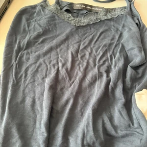 Mörkblå linnetopp med spetsdetalj - Säljer en mörkblå linnetopp från The Black Label Collection i storlek M. Toppen har tunna axelband och en snygg spetskant upptill som ger en extra touch. Perfekt att styla med jeans eller kjol för en trendig look🩷