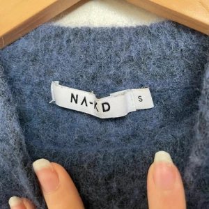 Blå fluffig stickad ull/mohair-tröja från NA-KD  - Mysig blå stickad tröja från NA-KD med hög hals och lång ärm. Tröjan är fluffig och tillverkad i en blandning av ull och mohair för extra värme och mjuk känsla. Perfekt för lager-på-lager under kyliga dagar.