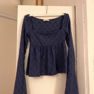 Blå långärmad blus från Nelly - Supersöt blå blus från Nelly med långärmad design och utsvängda ärmar. Toppen har ett diskret hålmönster och markerad midja som ger en fin siluett. Perfekt för dig som gillar romantiska detaljer och vill ha något unikt i garderoben. Endast använd 2 gånger alltså så gott som ny 💕passar även xs