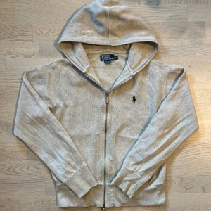 Beige hoodie från Polo Ralph Lauren - Beige hoodie från Polo Ralph Lauren med dragkedja och klassisk broderad logga på bröstet. Perfekt för en chill och stilren look. Den passar dig som är ca 170 cm lång. Skick: 7/10✅Fråga vid minsta fundering, pris kan diskuteras