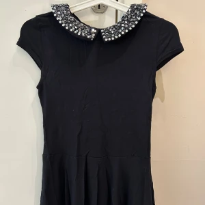 Svart topp  med paljettkrage - Supersöt svart topp  från New Look med glittrig paljettkrage och korta ärmar. Toppen  har lätt utställd form och tyget är mjukt och bekvämt. Perfekt för dig som vill sticka ut med en snygg detalj vid halsen.