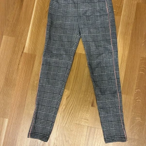 Rutig byxa från Lindex Kids 134/140 - Snygga smala byxor från Lindex Kids i svartvitt rutigt mönster med en rosa rand längs sidorna. Byxorna är i lite  stretchigt material och har en klassisk, smal passform. Perfekta för dig som gillar stilrena och trendiga plagg. Från djur-rök och parfymfritt hem! Fina men något noppriga. 