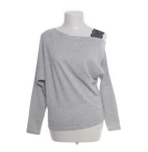 Grå offshoulder topp från Bodyflirt - Snygg grå långärmad topp från Bodyflirt i offshoulder-modell med en svart spetsdetalj vid axeln. Tunn och mjuk bomullskänsla, perfekt för dig som gillar avslappnad stil med en twist. Passformen är loose och toppen har en enkel, modern look.