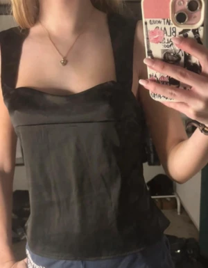 Svart omlott korsett-topp med knyt - Säljer en svart korsett-inspirerad topp med breda axelband och snygg omlott-design i ryggen. Toppen har knytband bak för att justera passformen och en stilren, croppad look. Materialet känns lätt och har en matt finish. Perfekt för dig som gillar trendiga och edgy plagg.