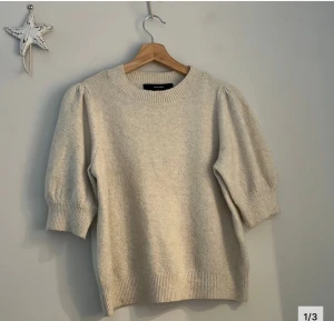 Beige stickad tröja Vero Moda - beige stickad tröja från Vero Moda med puffade halvlånga ärmar och bred ribbad kant vid hals, ärmslut och nederkant. 