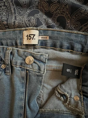 Blå skinny jeans från 157, storlek S, högmidjade  - Säljer ett par klassiska blå skinny jeans från 157 i modellen Snake. Byxorna har hög midja, dragkedja och knapp framtill samt fem fickor. Perfekta för dig som gillar en tight passform och enkel stil.