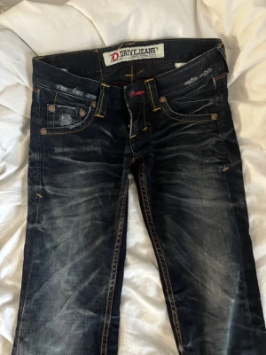 DriveJeans mörkblå jeans med kontrastsömmar - Mörkblå jeans från DriveJeans med slitna detaljer och tydliga kontrastsömmar i gult och rött. Klassisk femficksmodell med unika detaljer på bakfickan och en ljus denim patch. Snygg tvätt och coola färgskiftningar ger ett streetigt intryck.Pris går att diskutera❣️