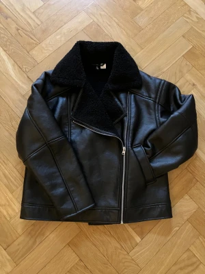 Svart teddyjacka från H&M Divided - Säljer min helt oanvända svarta biker/teddyjacka från H&M Divided i storlek S. Jackan har en bred krage i teddy, asymmetrisk dragkedja och två sidofickor. Yttermaterialet är i syntet med en matt finish och insidan är fodrad med mjuk teddy. Perfekt för kalla dagar🌸❄️