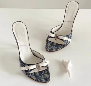 Blå och vita mönstrade pumps - Snygga pumps med blått och vitt mönster, spetsig tå och öppen tå. Skorna har en vit rem med metallspänne framtill och hög klack. Materialet ser ut att vara textil med inslag av syntet. Perfekta för dig som gillar statement skor med cool design.