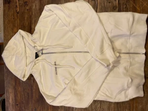 Vit hoodie - Vit hoodie med dragkedja. Tröjan har huva med snörning, ribbade muddar och lång ärm. Materialet känns som mjuk bomull och passformen är normal. 